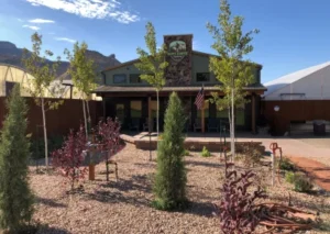 Exterior view of the Happy Camper building with a stone chimney, landscaped desert garden, and American flag