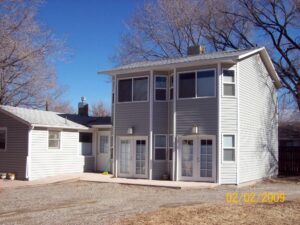 A two-story grey siding home addition featuring two sets of white double glass doors and multiple sliding windows