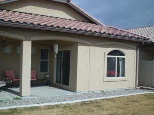 The rear exterior of a tan stucco home featuring a covered patio area and a large arched window