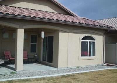 The rear exterior of a tan stucco home featuring a covered patio area and a large arched window