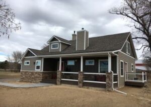 A brown single-story house with a grey shingle roof, stone veneer accents, and a wide covered front porch