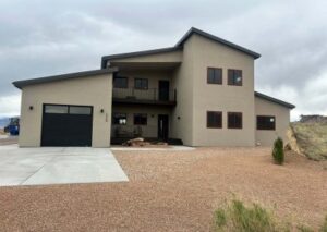 A modern tan two-story house with a black garage door, multiple brown-trimmed windows, and a second-story balcony