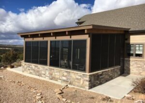 A modern screened-in porch with a stone veneer base and dark metal frames, attached to a house overlooking a desert landscape